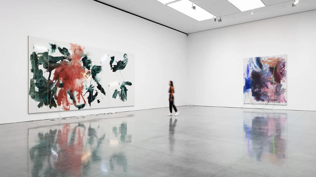 A visitor walking through a Gagosian gallery, large gestural abstract canvases on the white walls reflected in the polished concrete floor.