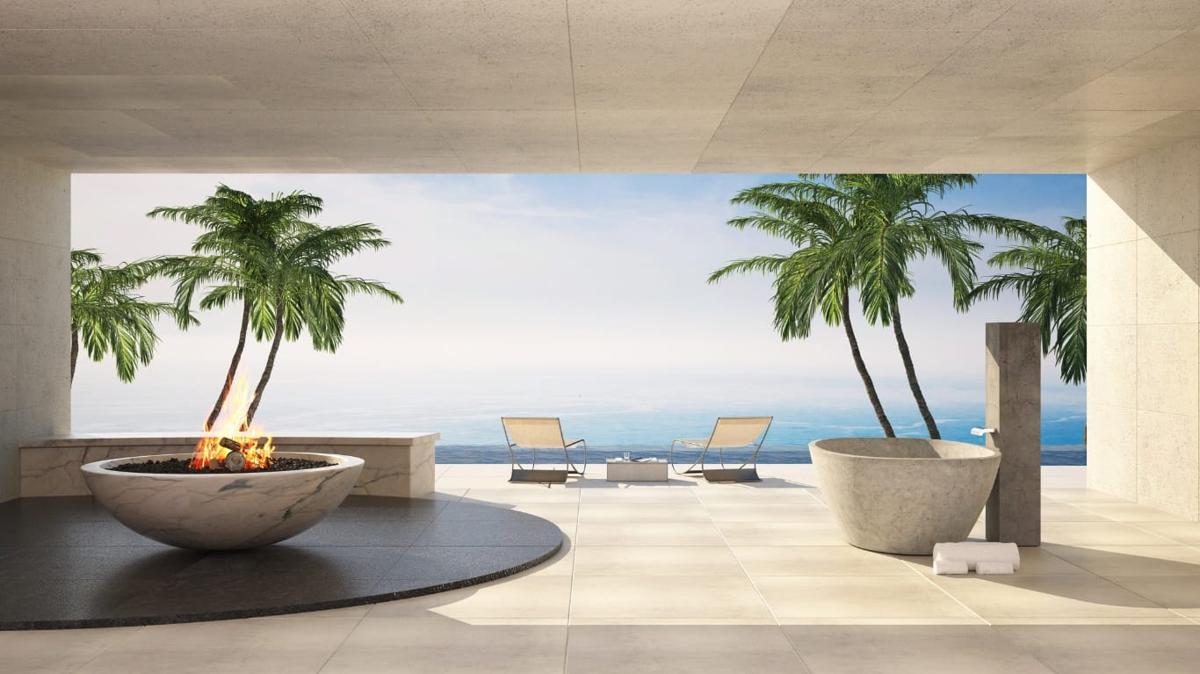 A stone terrace of a luxury residence with a marble fire bowl, a carved stone bathtub and lounge chairs facing palms and the sea.