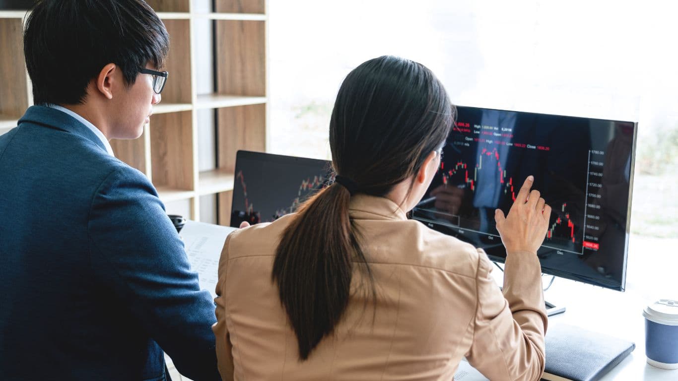 A woman is explaining the concept of a Couch-Potato Portfolio to a young investor as they both focus on a chart displayed on the computer