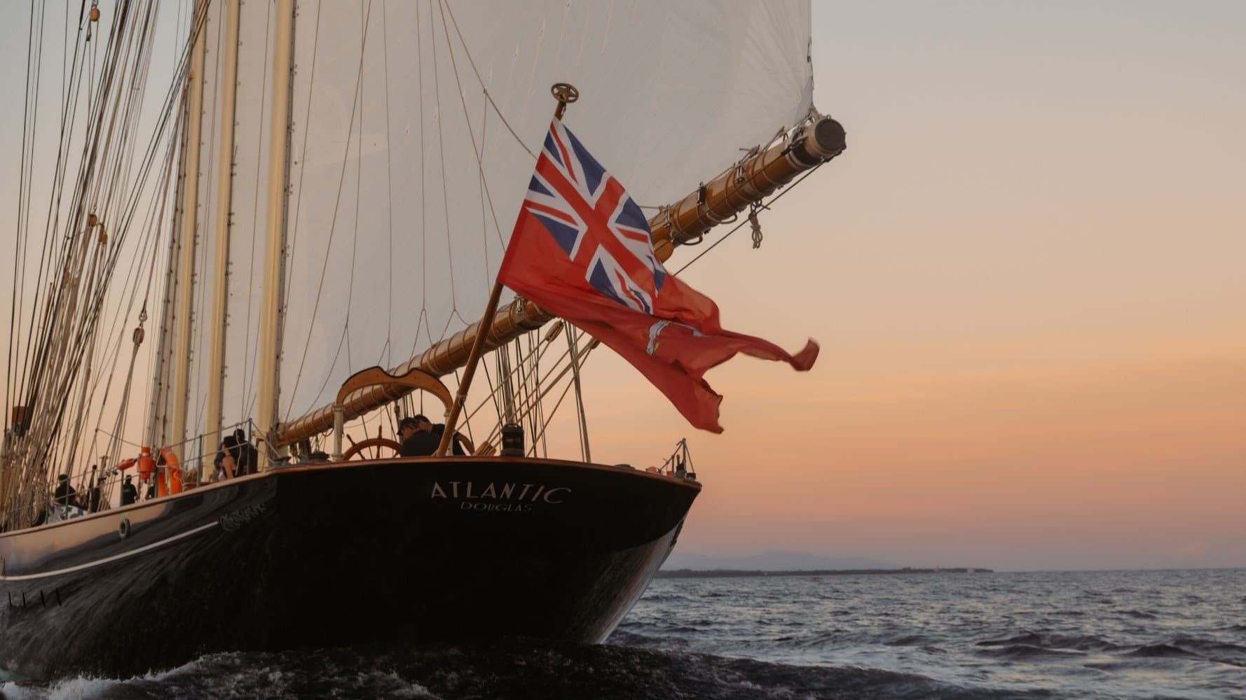 The bow of ATLANTIC, the 65-metre Bernard Gallay schooner replica, with the British red ensign flying in late Mediterranean light — the iconic image of classical sailing yacht ownership in the modern superyacht era.