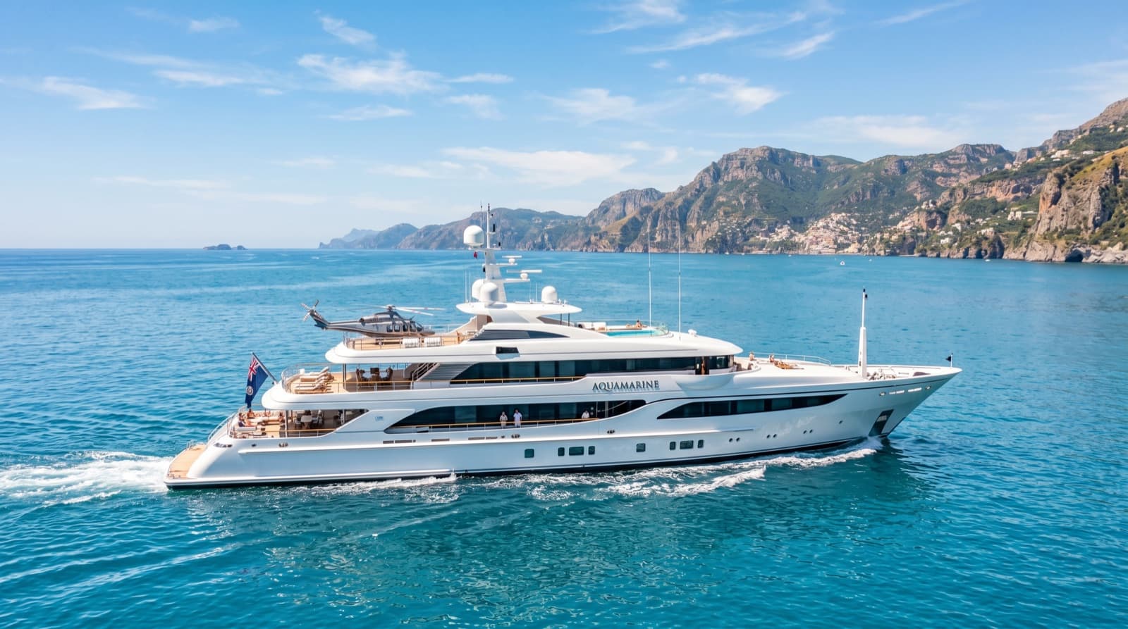 A large white superyacht cruising past a mountainous Mediterranean coastline