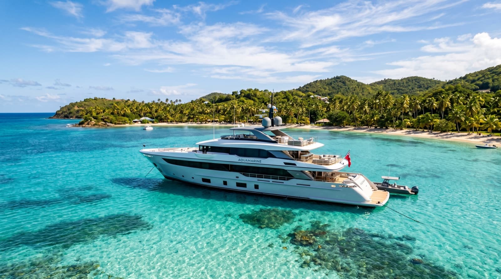 A white superyacht at anchor in clear turquoise water beside a tropical island
