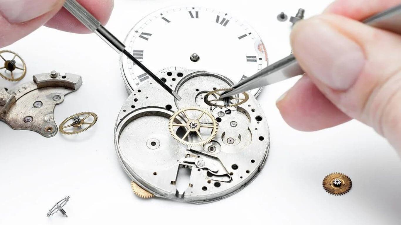 A watchmaker servicing a disassembled mechanical watch movement with tweezers and a fine screwdriver.