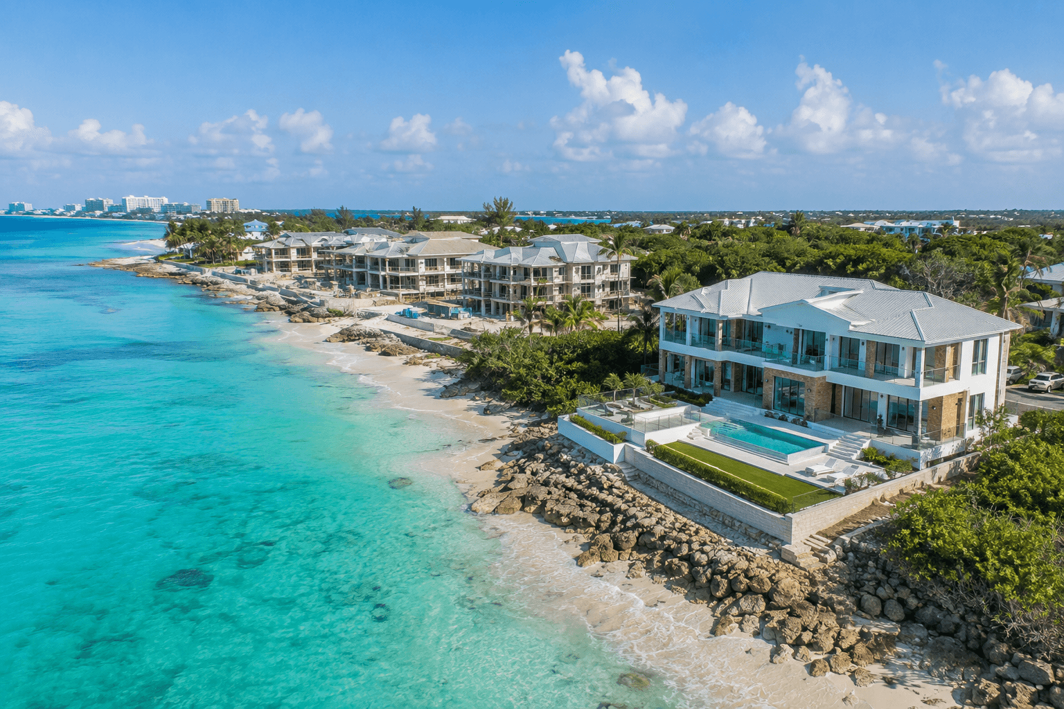 Luxury residences under construction beside completed waterfront property on the turquoise Grand Cayman coastline.