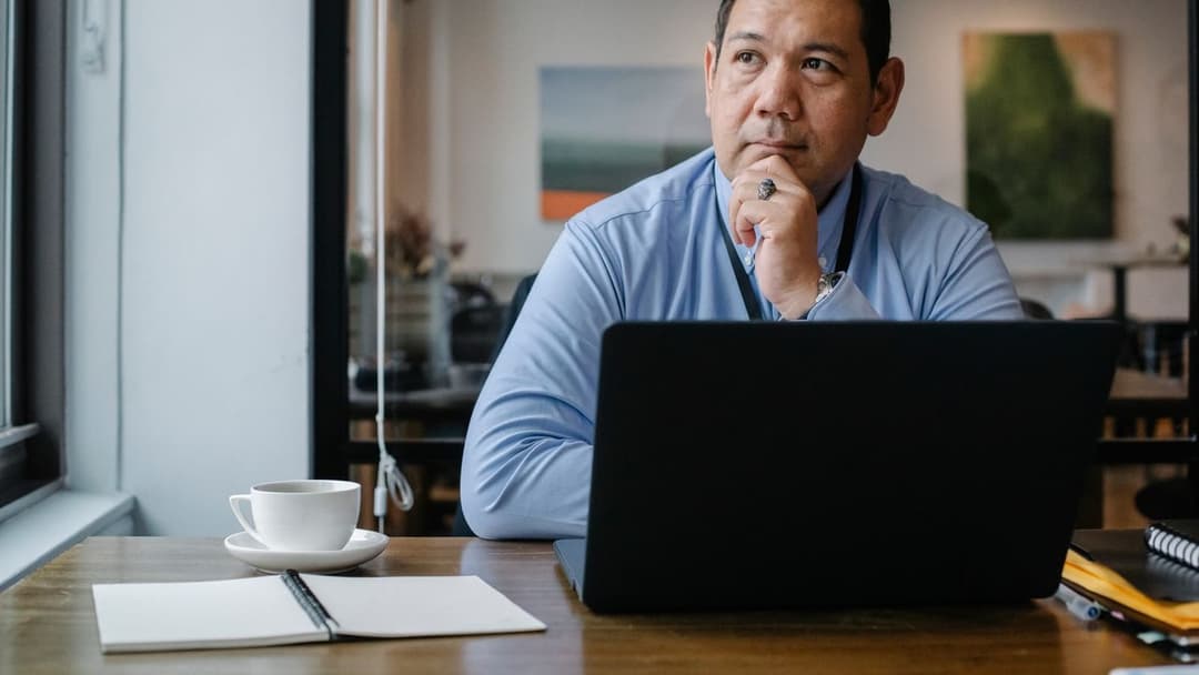 A wealth professional pauses at his desk, hand to chin, deliberating rather than reacting — the calm, unhurried judgment behind fortunes that last.