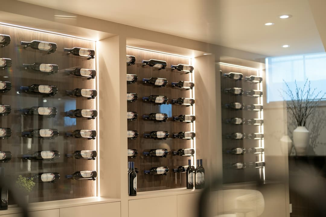 A modern wine cellar wall with illuminated racks of display bottles behind glass, ownership arranged to be seen.