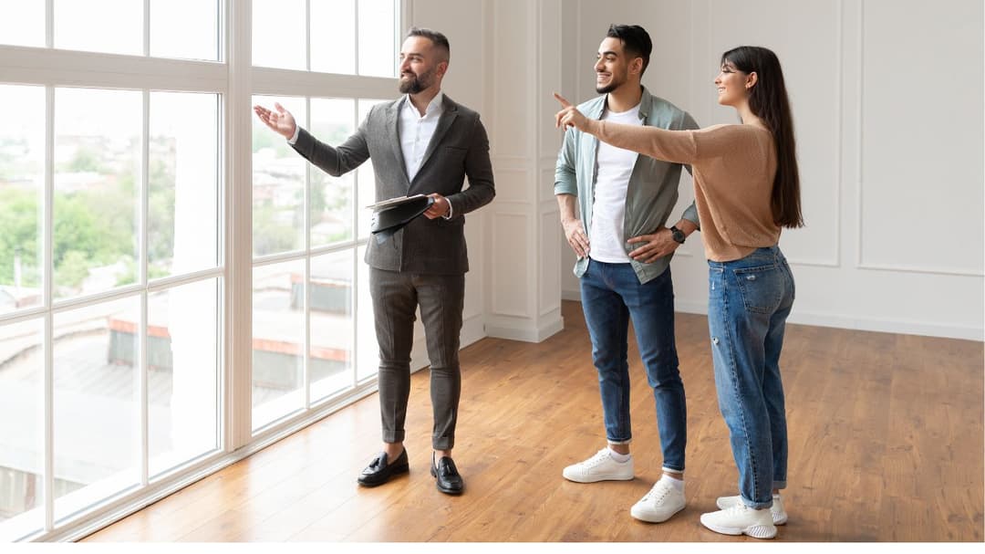 A professional real estate agent in a tailored suit is showing a young couple the stunning view from the house, enthusiastically highlighting the property's unique features and the surrounding landscape.