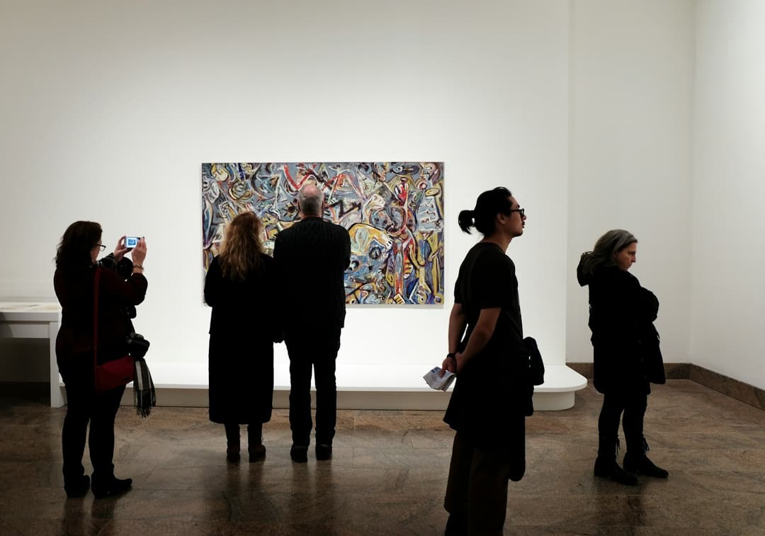 Visitors standing before a large abstract painting in a white walled gallery.