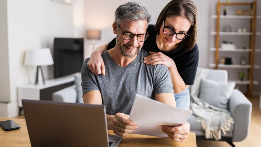 A couple reviewing their options for opening an IRA, with paperwork in hand and a laptop nearby for research.