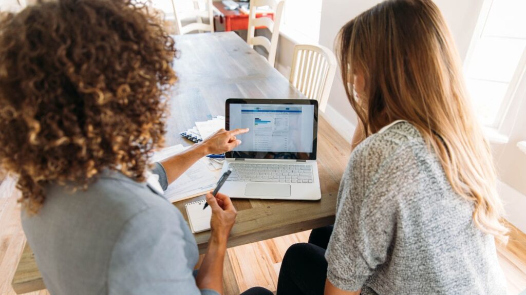 A financial advisor and their client sit side by side, intently reviewing options on a laptop, illustrating potential investment strategies and financial goals.