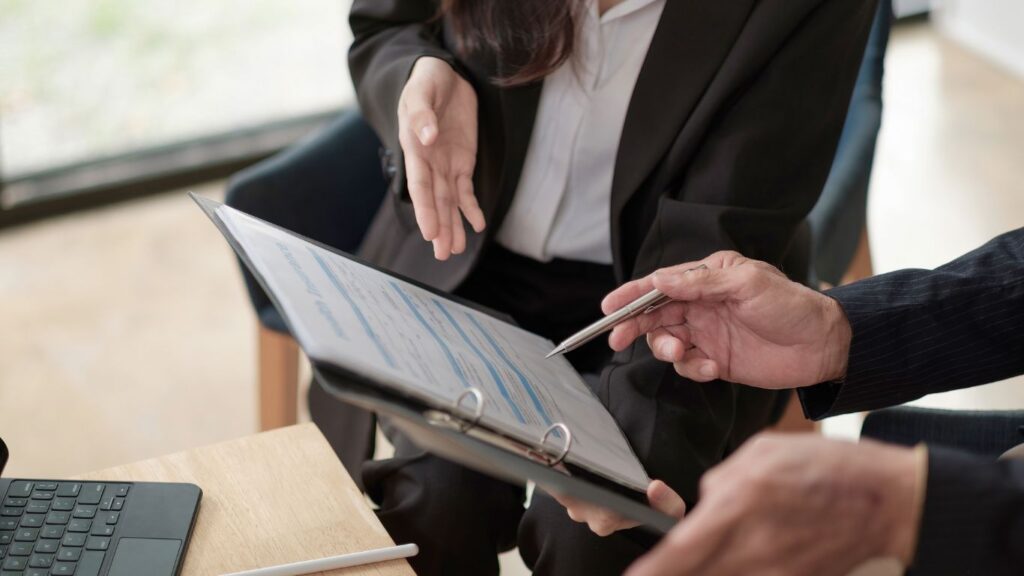 A financial advisor and a client are engaged in a lively conversation, both holding the same folder. They lean in closely, pointing at financial statistics and charts as they discuss insights and strategies, fostering a collaborative and dynamic atmosphere.