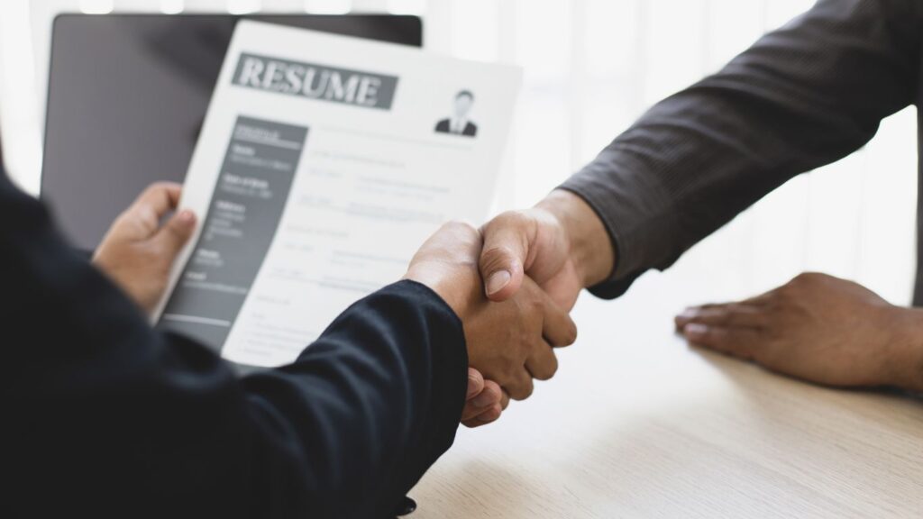 Two men shaking hands after a job interview, with one holding the resume in his other hand