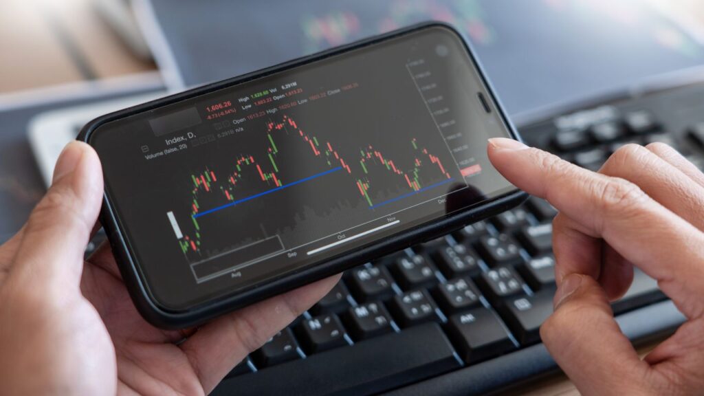 A person holding a cellphone, showing a stock chart on the screen