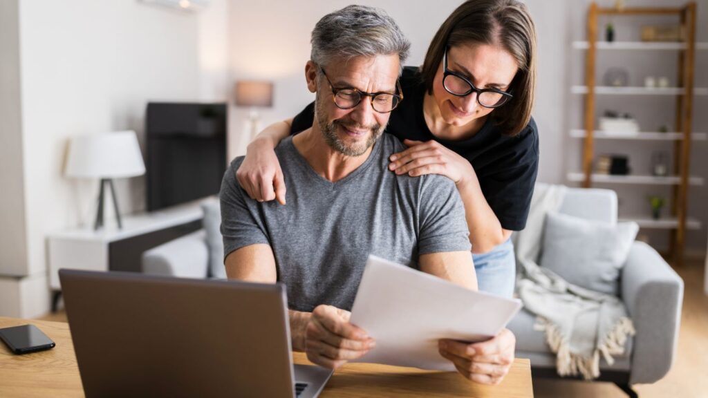 A couple reviewing their options for opening an IRA, with paperwork in hand and a laptop nearby for research.