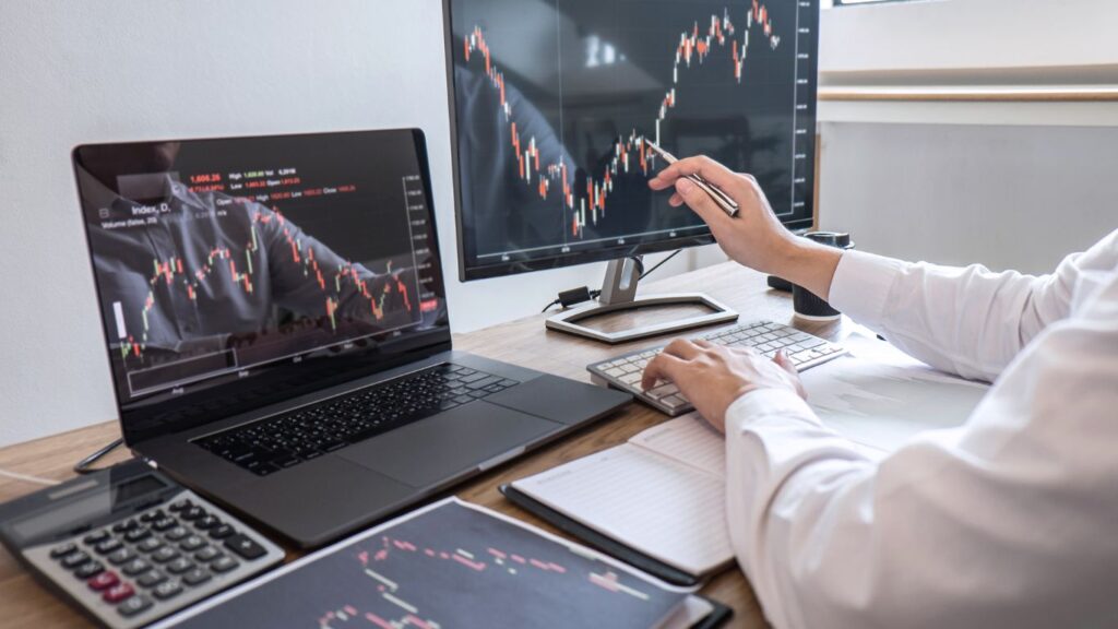 A trader sits focused in front of a laptop and monitor, both displaying complex charts, deeply analyzing Index Rebalancing strategies