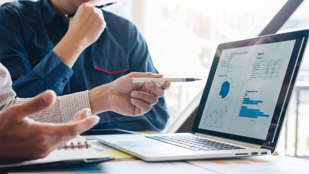 Two individuals are seated in front of a laptop, with one person actively explaining to the other the importance and necessity of Index Rebalancing